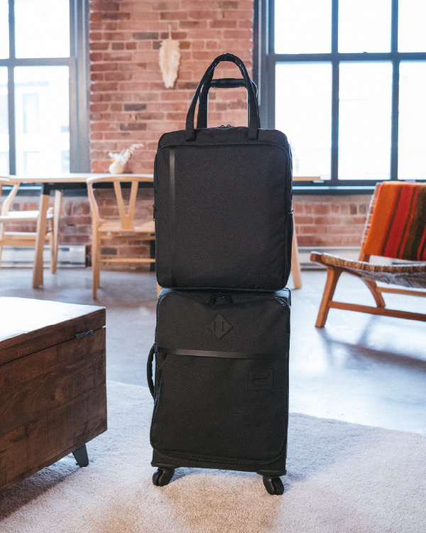 A Highland Luggage Carry-On in Black with a Travel Tote on top of it.